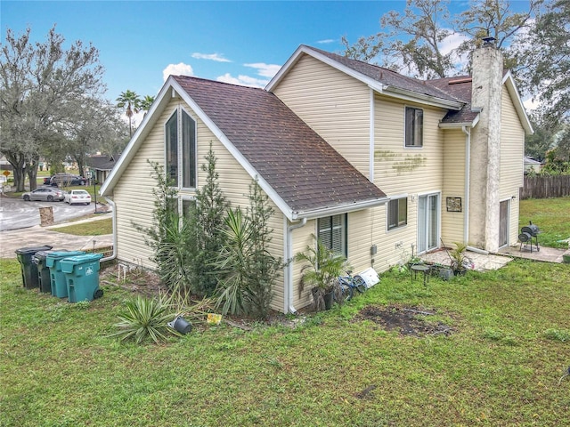 back of house with a yard, a shingled roof, a chimney, and fence