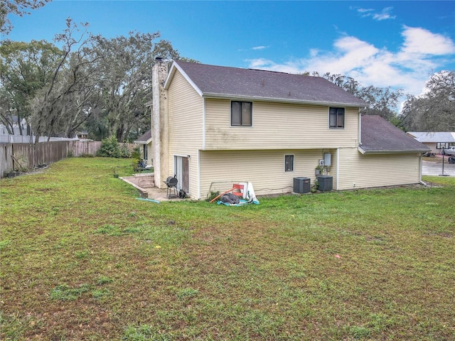 rear view of property featuring a lawn, a chimney, cooling unit, and fence