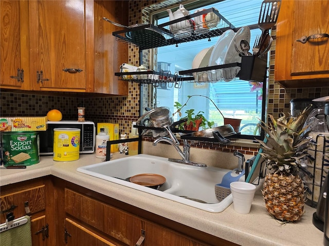 kitchen with a sink, light countertops, brown cabinetry, and backsplash