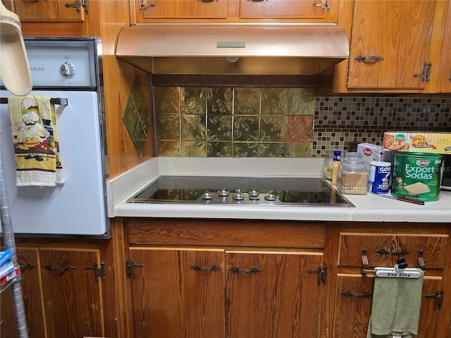 kitchen featuring brown cabinetry, decorative backsplash, white oven, light countertops, and black electric cooktop