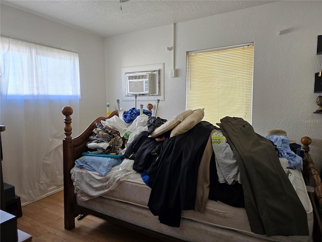 bedroom featuring a textured wall, an AC wall unit, a textured ceiling, and wood finished floors