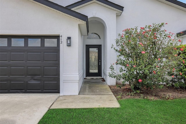 doorway to property featuring a garage, concrete driveway, and stucco siding