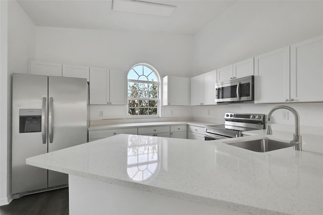 kitchen with white cabinets, appliances with stainless steel finishes, light stone counters, a peninsula, and a sink