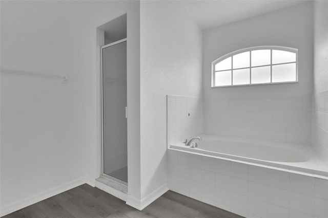 full bathroom featuring a stall shower, wood finished floors, a bath, and baseboards