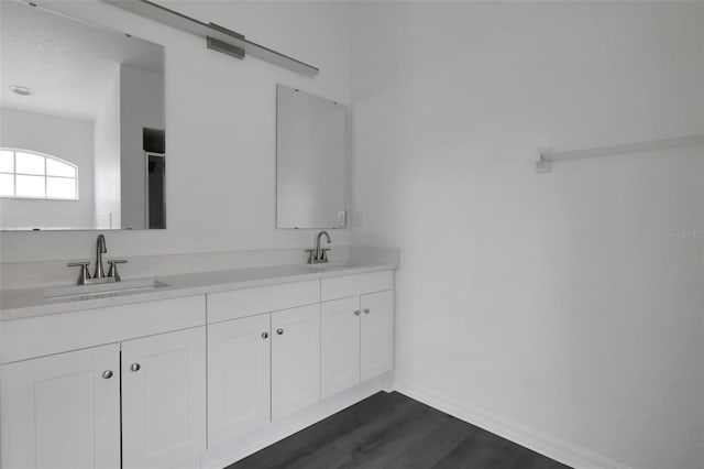 bathroom with double vanity, wood finished floors, a sink, and baseboards