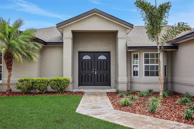 view of exterior entry featuring a yard, stucco siding, and roof with shingles