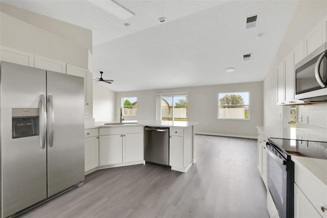 kitchen with a peninsula, a sink, visible vents, light countertops, and appliances with stainless steel finishes