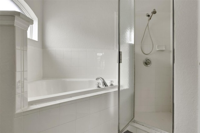 full bathroom with a textured wall, a shower stall, and a bath