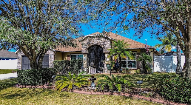 view of front of house featuring a garage, stone siding, fence, and a front yard