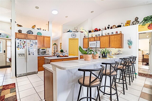 kitchen with white appliances, brown cabinets, a peninsula, and light tile patterned floors