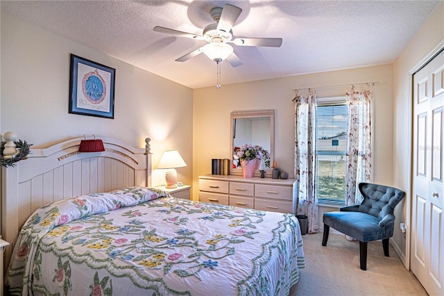 bedroom featuring a ceiling fan, a closet, light colored carpet, and a textured ceiling