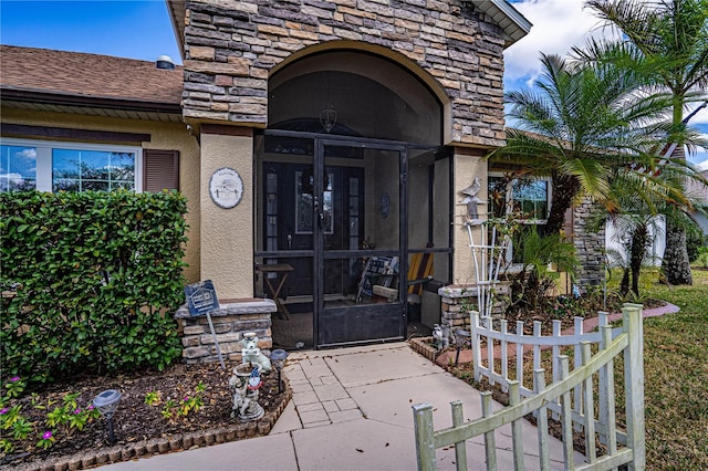 doorway to property featuring stone siding, roof with shingles, and stucco siding