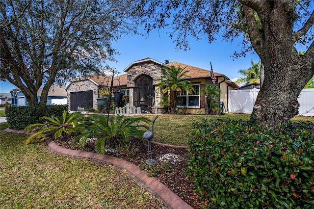 view of front of house with a gate, fence, a garage, stone siding, and a front lawn