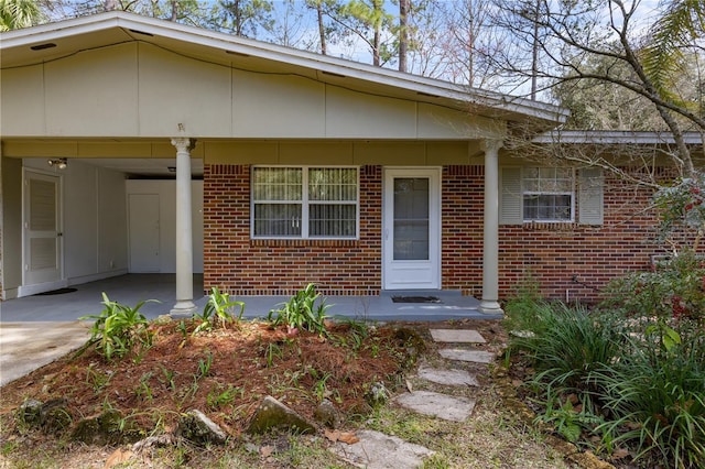 view of exterior entry featuring a porch, an attached carport, concrete driveway, and brick siding