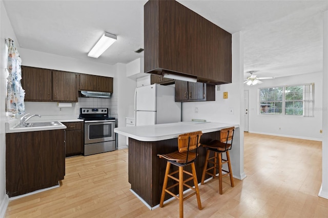 kitchen featuring electric range, a sink, freestanding refrigerator, and dark brown cabinetry