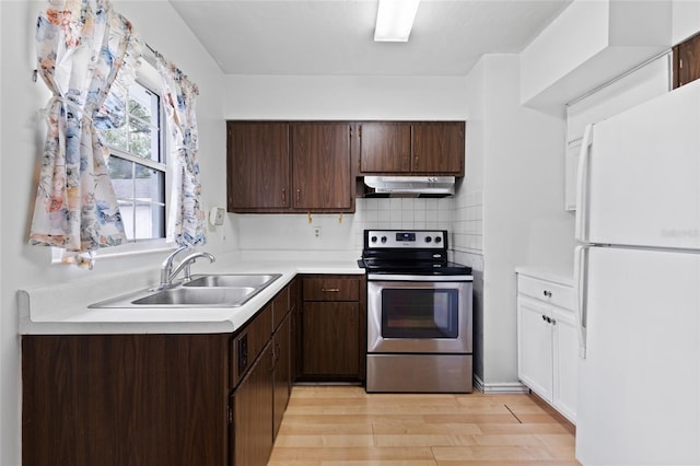 kitchen with electric stove, freestanding refrigerator, light countertops, under cabinet range hood, and a sink