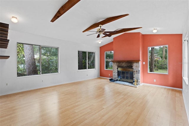 unfurnished living room with vaulted ceiling with beams, plenty of natural light, a glass covered fireplace, and light wood-style floors