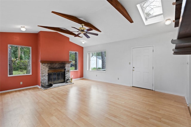 unfurnished living room with baseboards, vaulted ceiling with skylight, a brick fireplace, and light wood-style floors