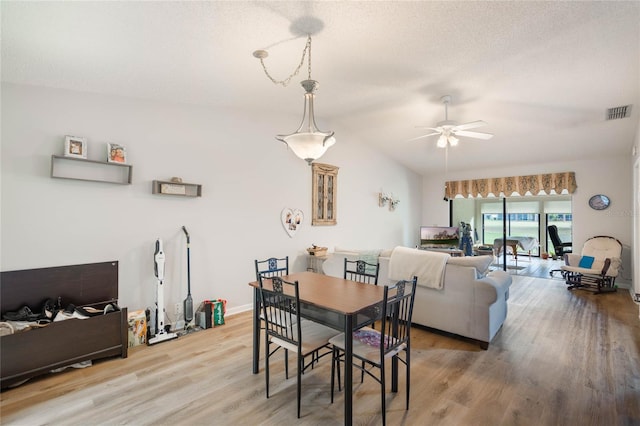 dining space featuring ceiling fan, a textured ceiling, wood finished floors, visible vents, and vaulted ceiling