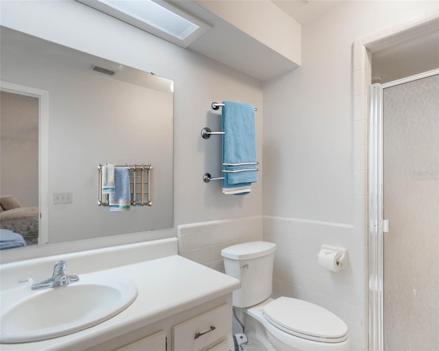 ensuite bathroom with toilet, a wainscoted wall, vanity, tile walls, and a shower stall