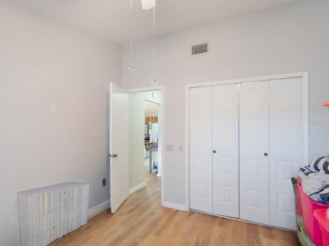 bedroom featuring light wood finished floors, a closet, visible vents, a textured ceiling, and baseboards