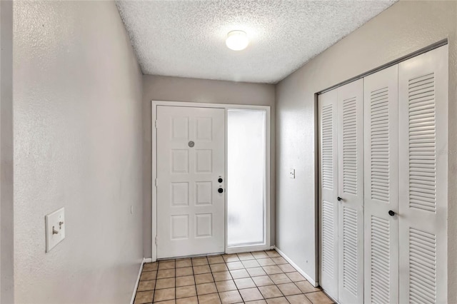 foyer entrance featuring a textured wall, baseboards, a textured ceiling, and light tile patterned flooring