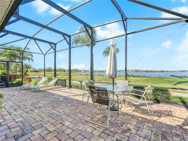 view of patio / terrace featuring outdoor dining area, glass enclosure, and a water view