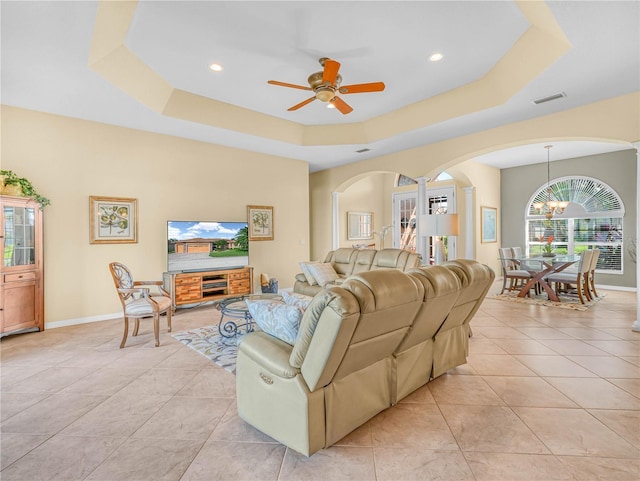 living room with light tile patterned floors, baseboards, visible vents, a raised ceiling, and ceiling fan with notable chandelier