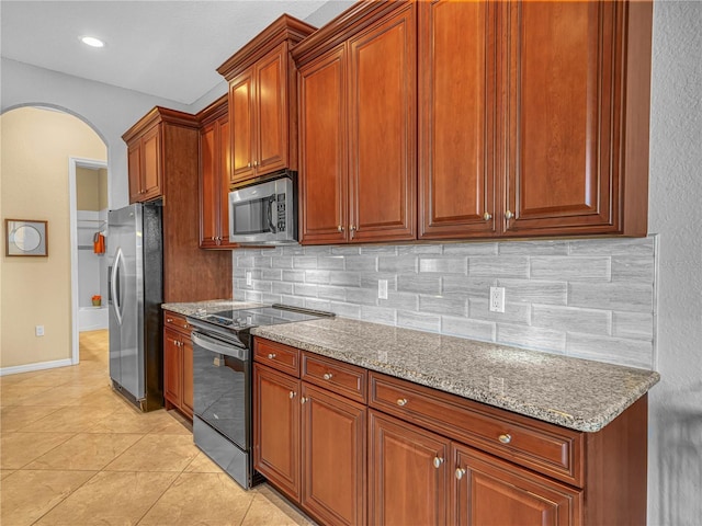 kitchen with arched walkways, light stone counters, stainless steel appliances, backsplash, and light tile patterned flooring