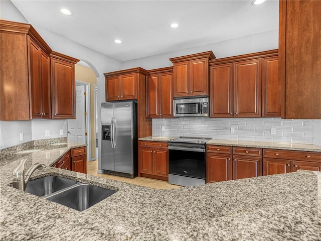 kitchen featuring recessed lighting, backsplash, appliances with stainless steel finishes, a sink, and light stone countertops