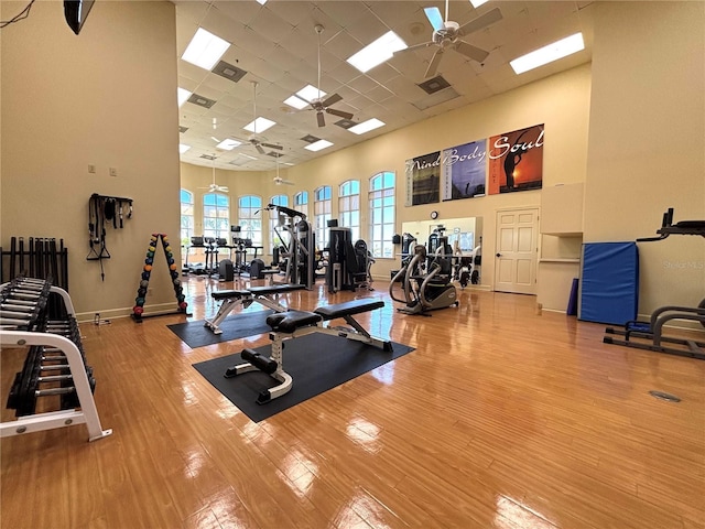 workout area with a towering ceiling, a paneled ceiling, wood finished floors, and a ceiling fan