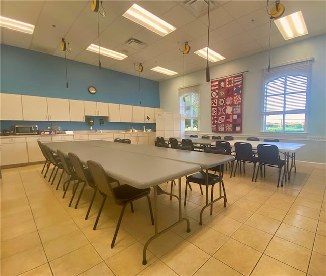 dining room with a high ceiling, visible vents, a drop ceiling, and light tile patterned flooring