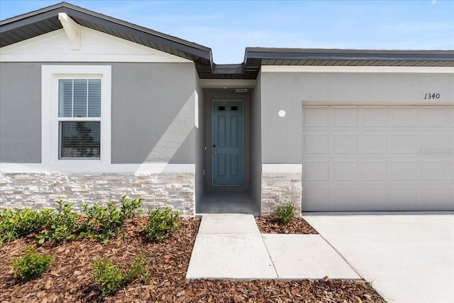 doorway to property featuring a garage, stone siding, and stucco siding