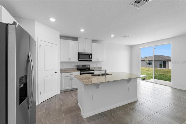 kitchen featuring a center island with sink, visible vents, appliances with stainless steel finishes, light stone counters, and a sink