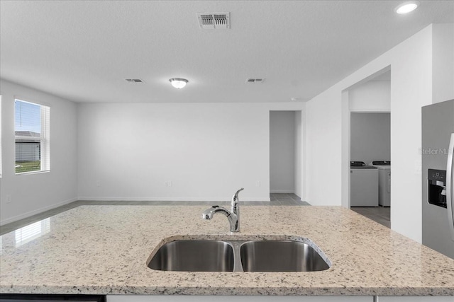 kitchen with visible vents, light stone counters, washing machine and clothes dryer, stainless steel refrigerator with ice dispenser, and a sink