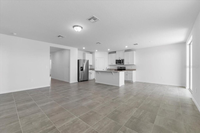 kitchen with stainless steel appliances, visible vents, white cabinetry, open floor plan, and an island with sink