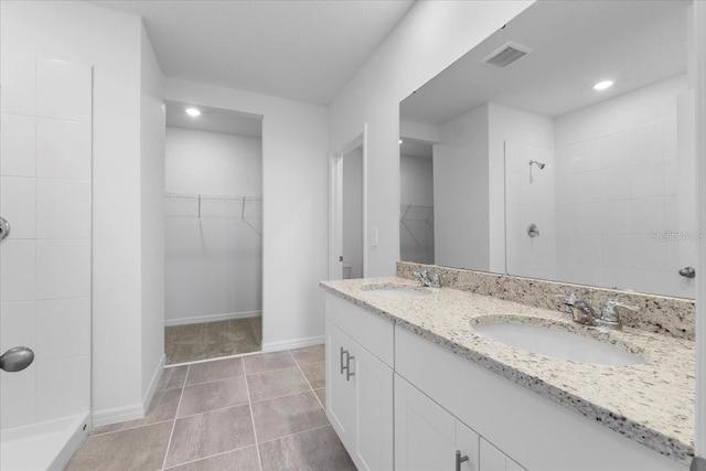 full bath featuring a tile shower, a sink, visible vents, and a walk in closet