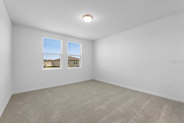 carpeted spare room with a textured ceiling and baseboards