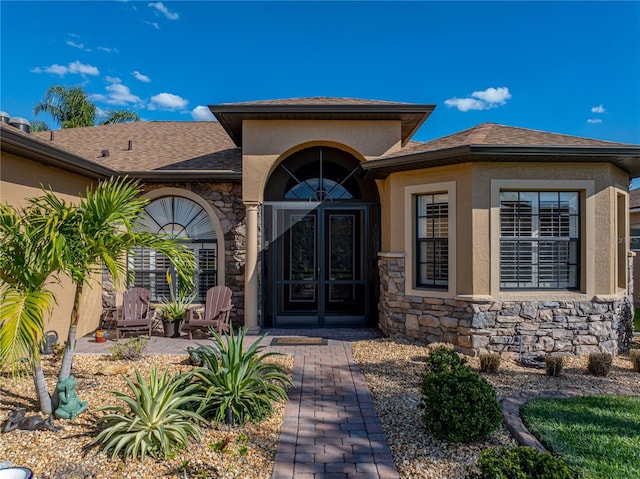 view of exterior entry with a shingled roof, stone siding, and stucco siding