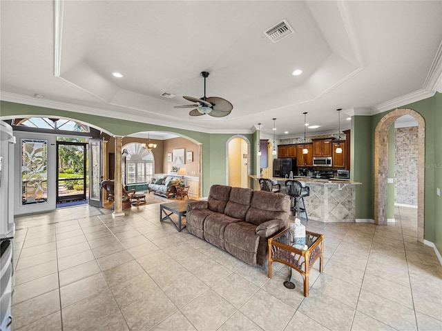 living area with light tile patterned floors, a tray ceiling, and arched walkways