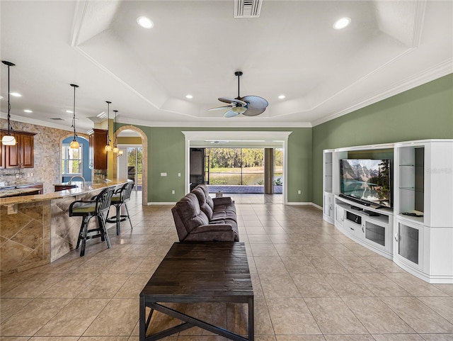 living area with arched walkways, visible vents, baseboards, a raised ceiling, and crown molding