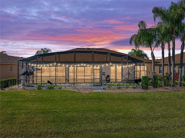 back of property at dusk featuring glass enclosure and a lawn