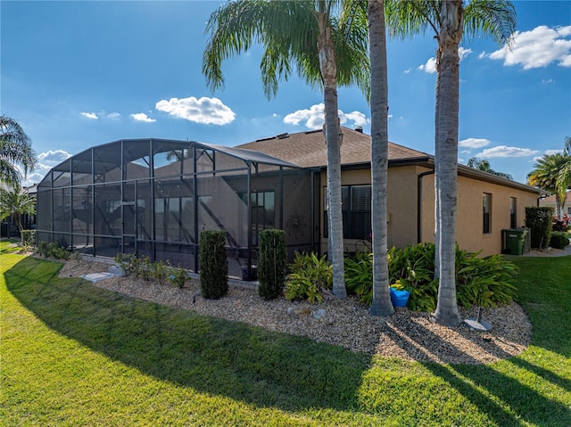 back of property with glass enclosure, a lawn, and stucco siding