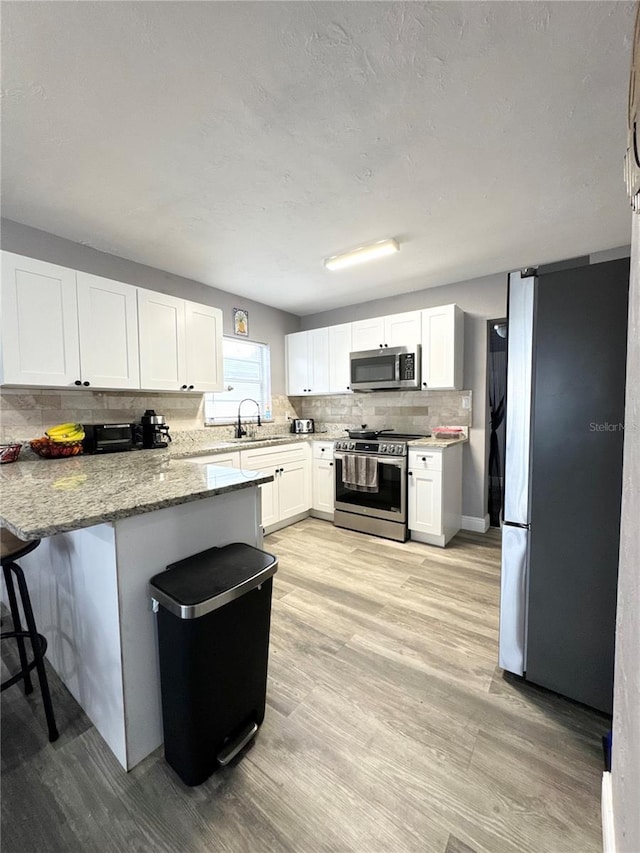 kitchen with appliances with stainless steel finishes, white cabinetry, a peninsula, and tasteful backsplash