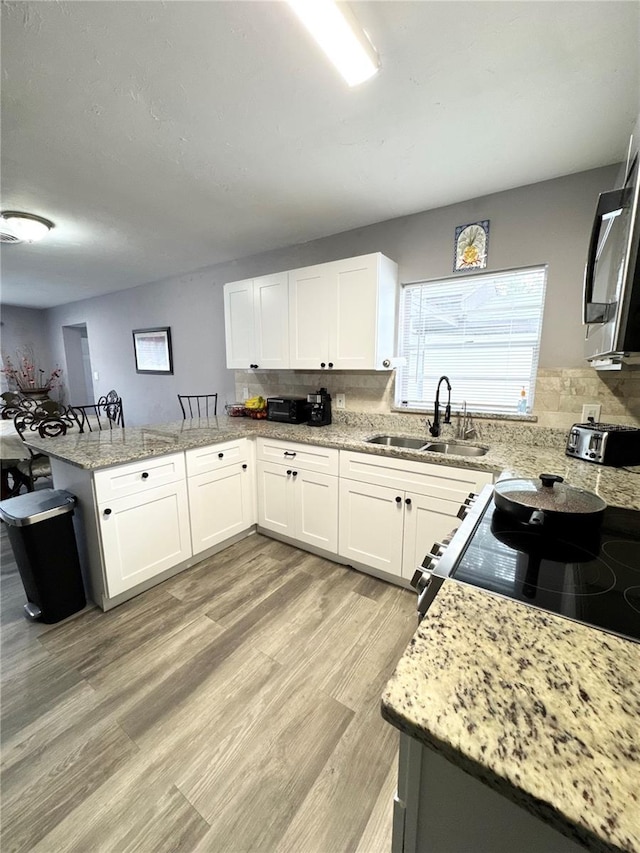 kitchen with light wood-style flooring, light stone counters, a peninsula, a sink, and backsplash