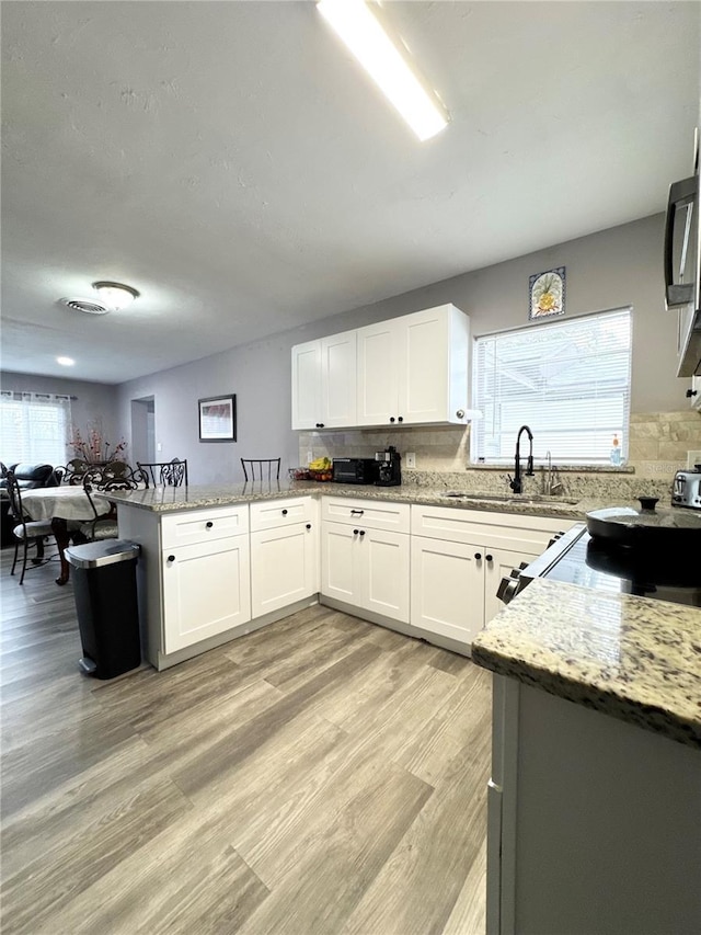 kitchen featuring a peninsula, backsplash, a sink, and light stone countertops