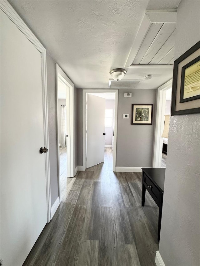 hallway featuring a textured ceiling, baseboards, and wood finished floors