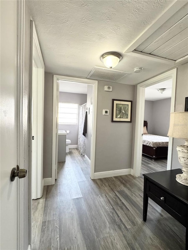 corridor with a textured ceiling, wood finished floors, and baseboards