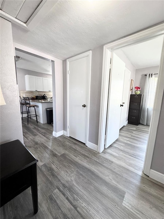 hall featuring a textured ceiling, wood finished floors, and baseboards