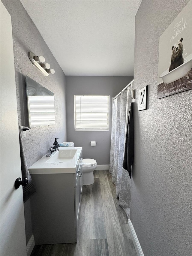 bathroom featuring a textured ceiling, a textured wall, toilet, wood finished floors, and vanity